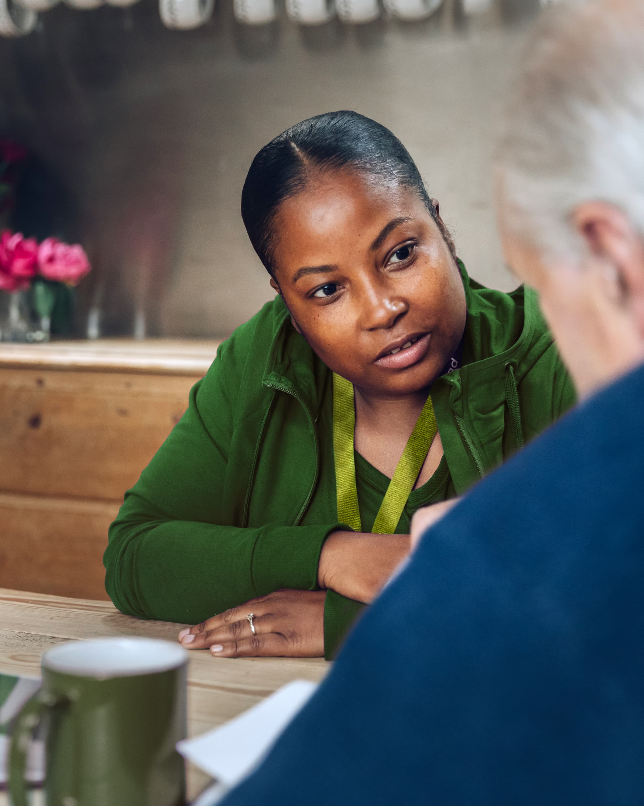 A woman in green talks intently with an older man at a table in a cozy setting. - Home Instead