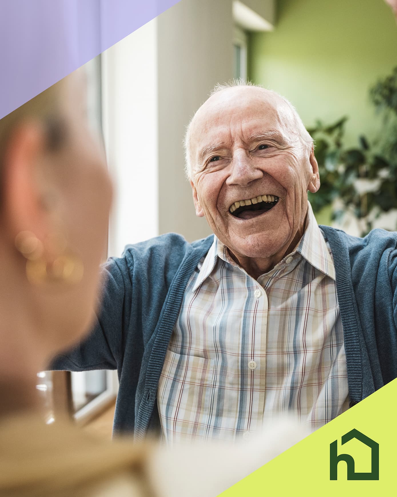 Smiling elderly man greeting someone indoors, with a green home logo in the bottom right corner. - Home Instead