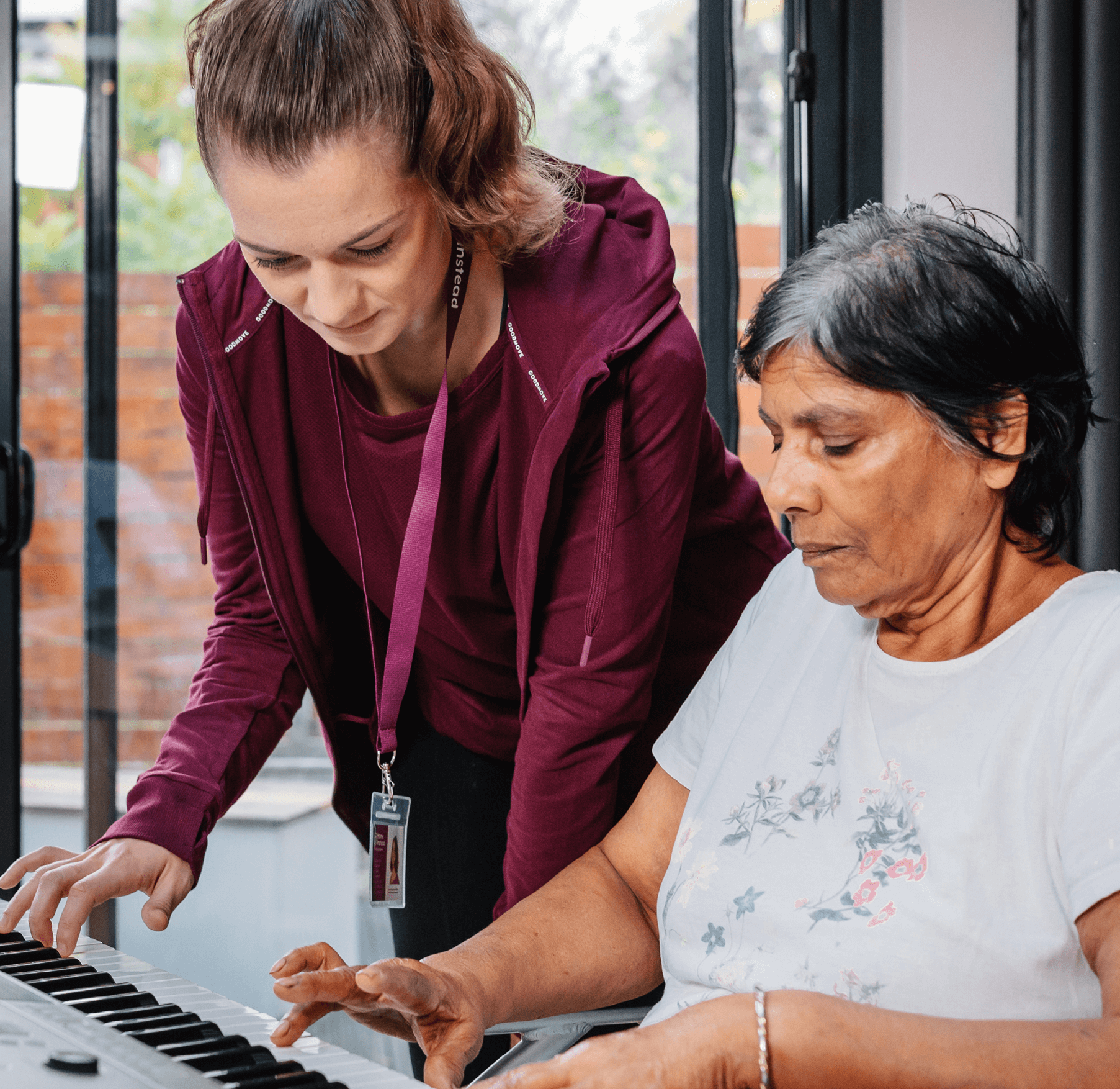 A caregiver assists an elderly woman in playing the keyboard, focusing on the keys together. - Home Instead