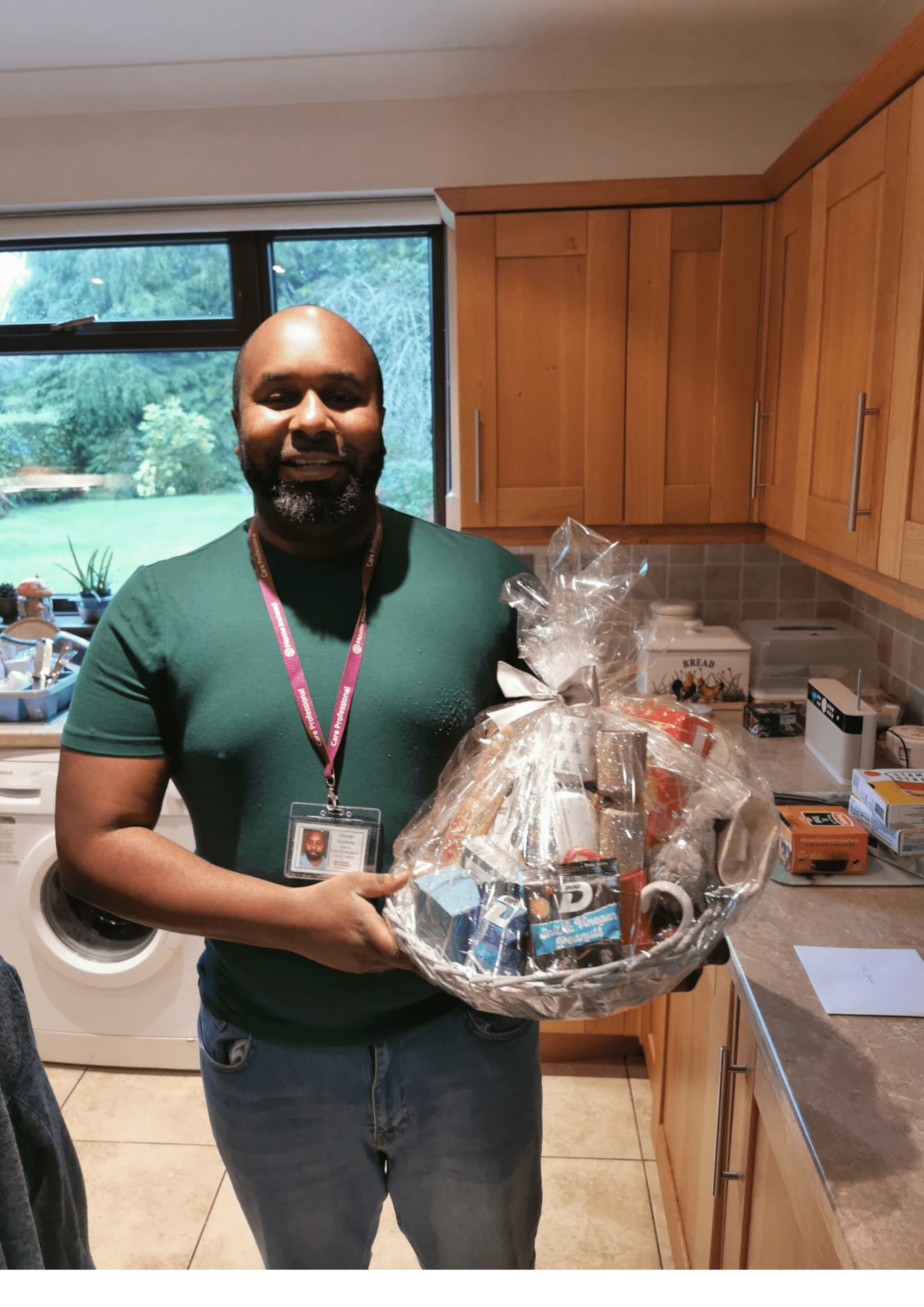 Woman in a gray sweater holding a smartphone and smiling while looking to the side, seated at a table. - Home Instead