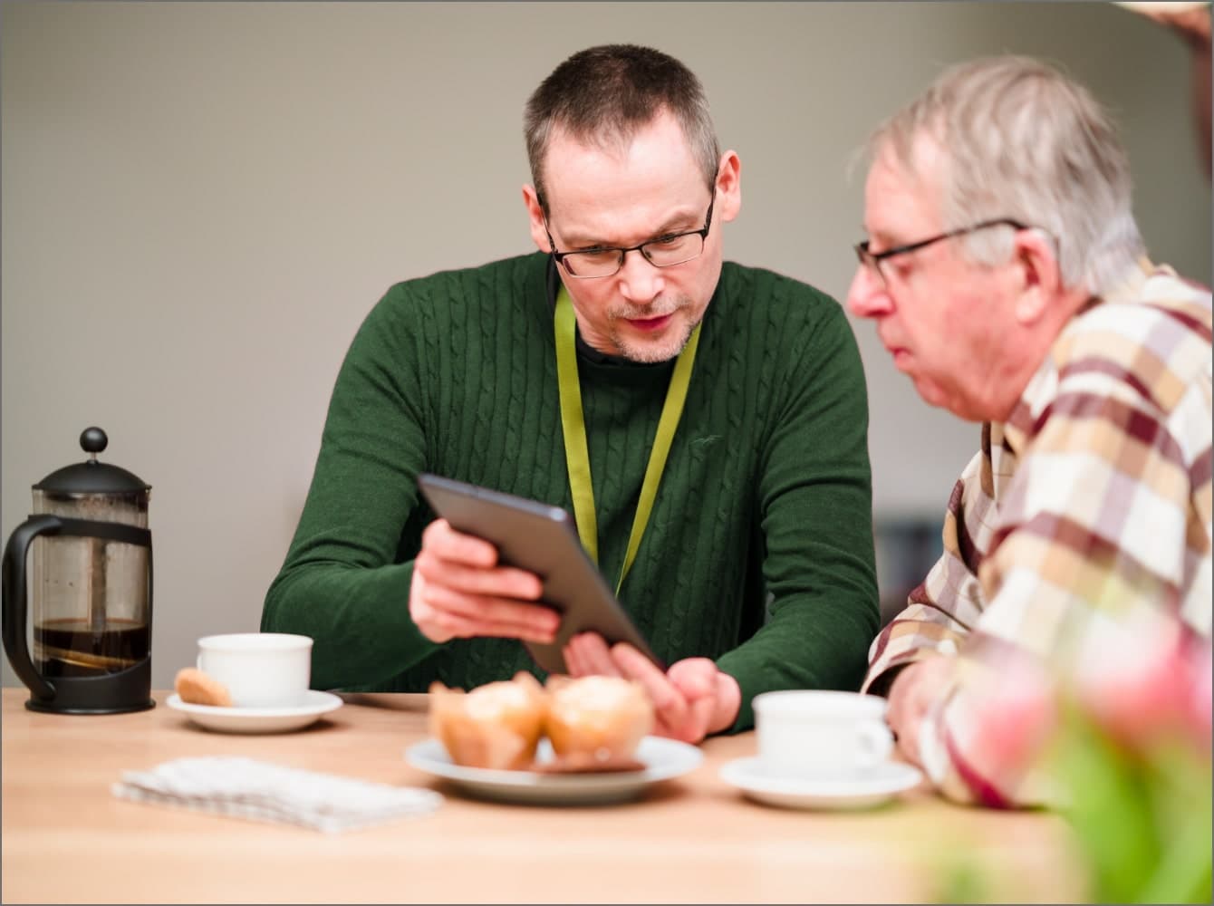 An elderly woman and a younger woman smile at each other while holding a magazine indoors. - Home Instead
