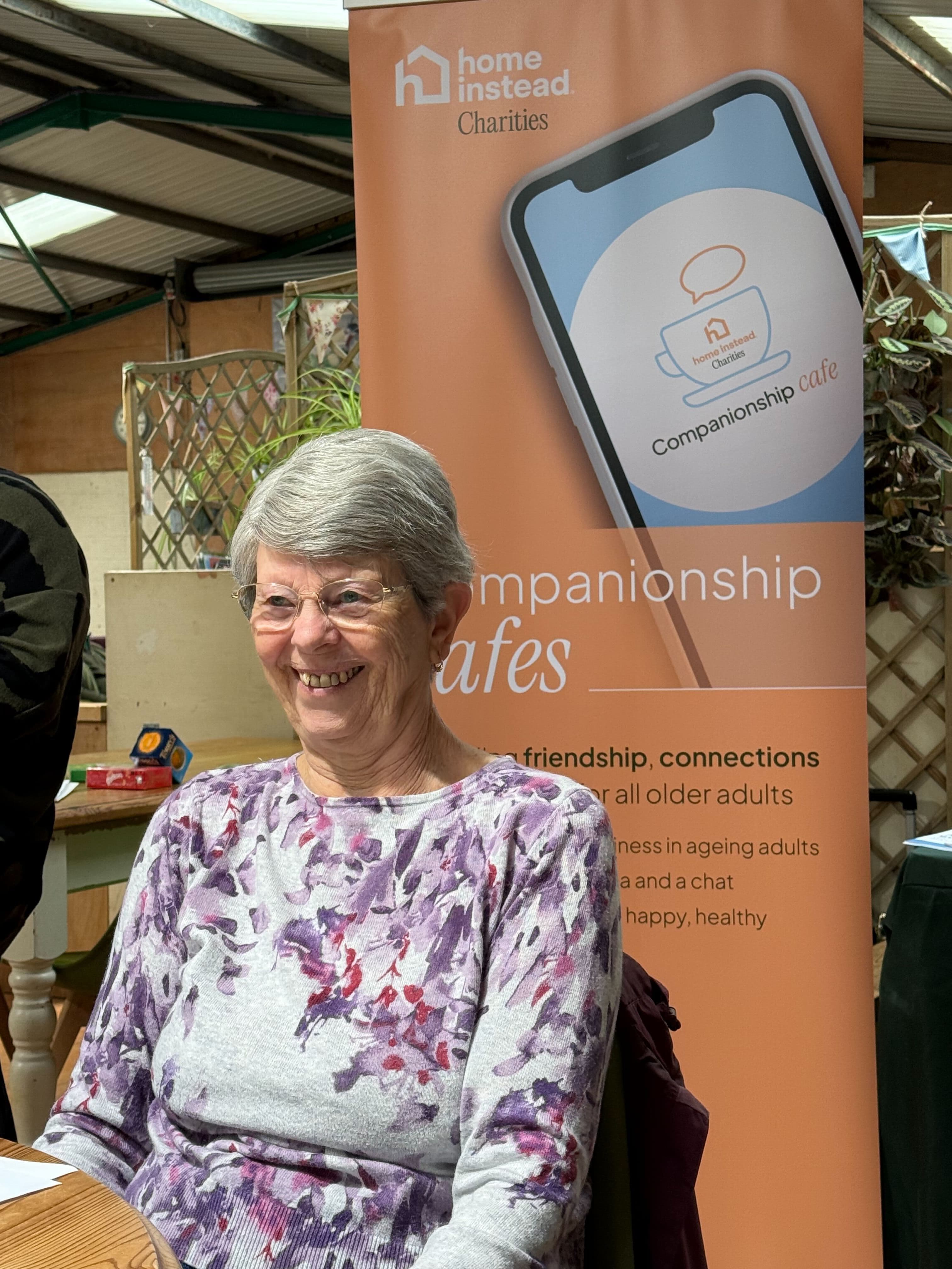 Woman sitting in front of a Home Instead Charities banner