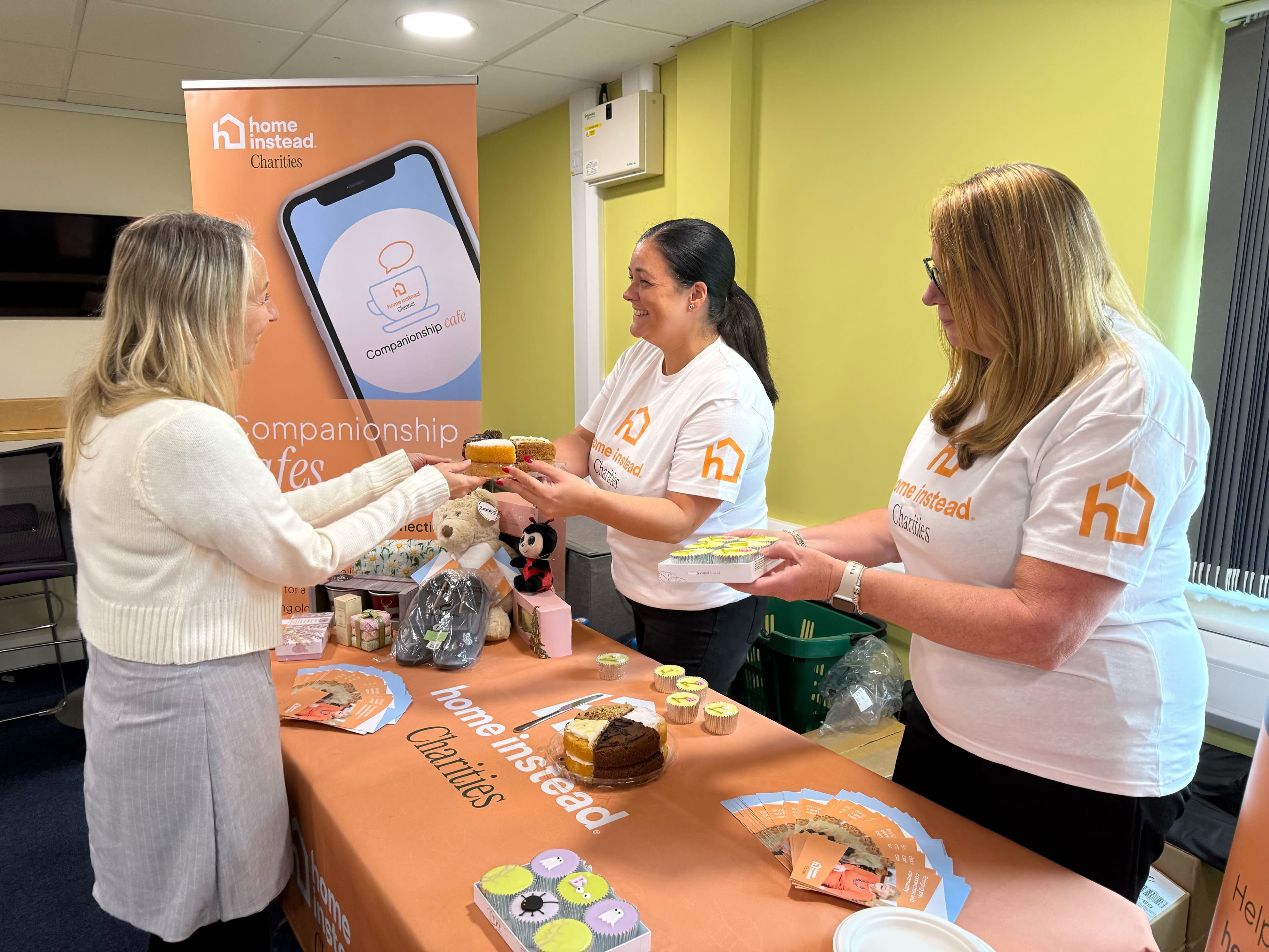 3 women around a Home Instead charities bake stall