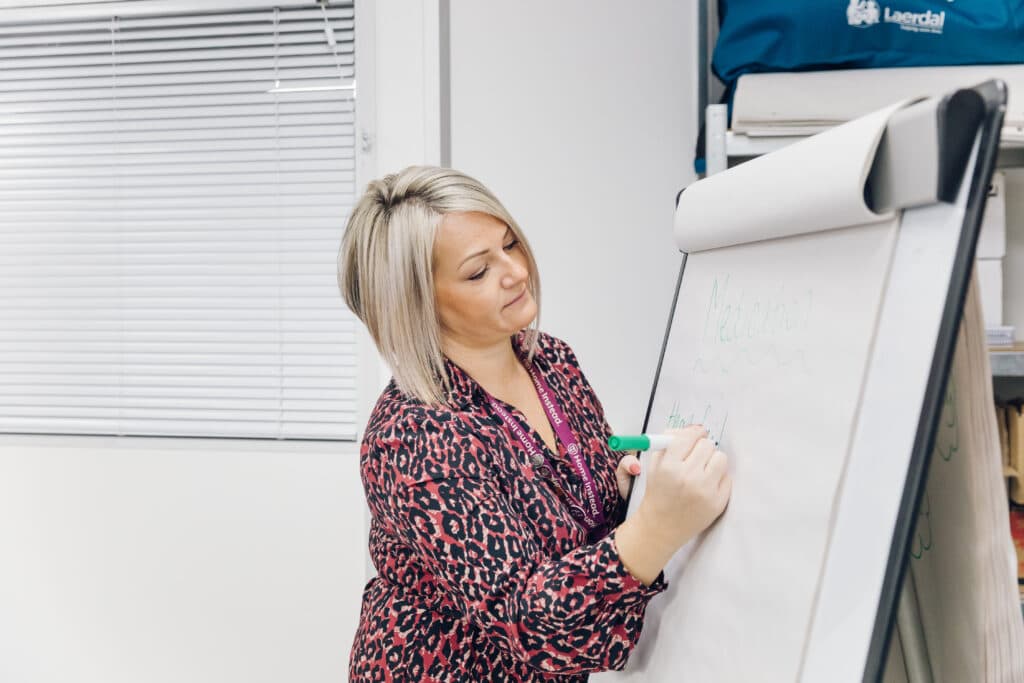 Woman writing on a flipchart with a green marker in a classroom or office setting. - Home Instead