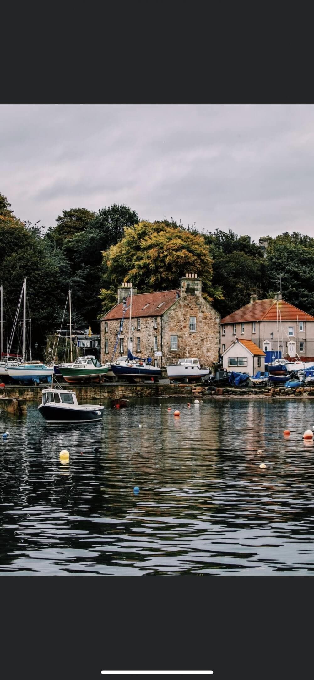 Quaint harbor with boats and scenic buildings, surrounded by lush trees and reflecting in the water. - Home Instead