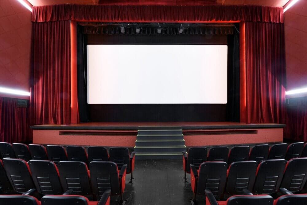 Empty movie theater with red curtains and a large blank screen, viewed from the seating area. - Home Instead