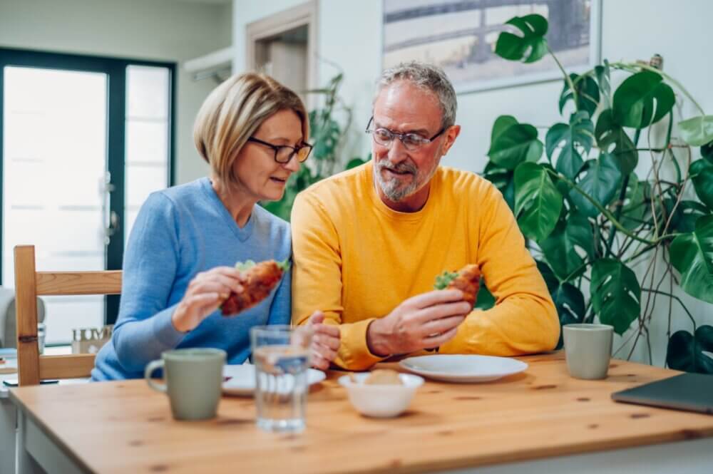 A man and woman sit at a table, holding tacos. They are surrounded by houseplants and have mugs, plates, and a laptop nearby. - Home Instead Southampton