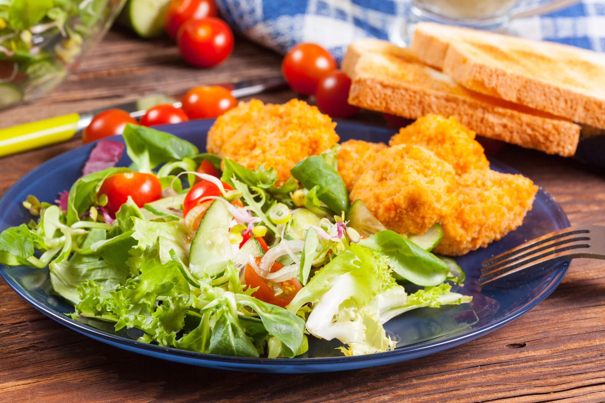 A blue plate with fried chicken, a fresh garden salad with cherry tomatoes and cucumbers, and slices of toasted bread. - Home Instead
