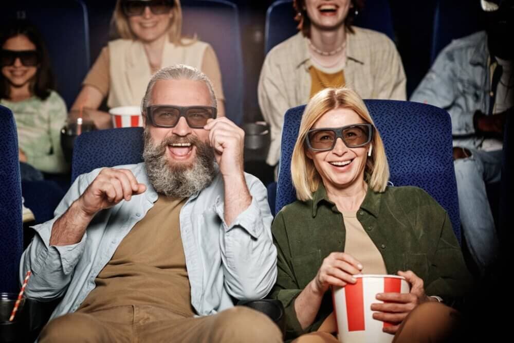 A group of people wearing 3D glasses, laughing and eating popcorn in a movie theater. - Home Instead