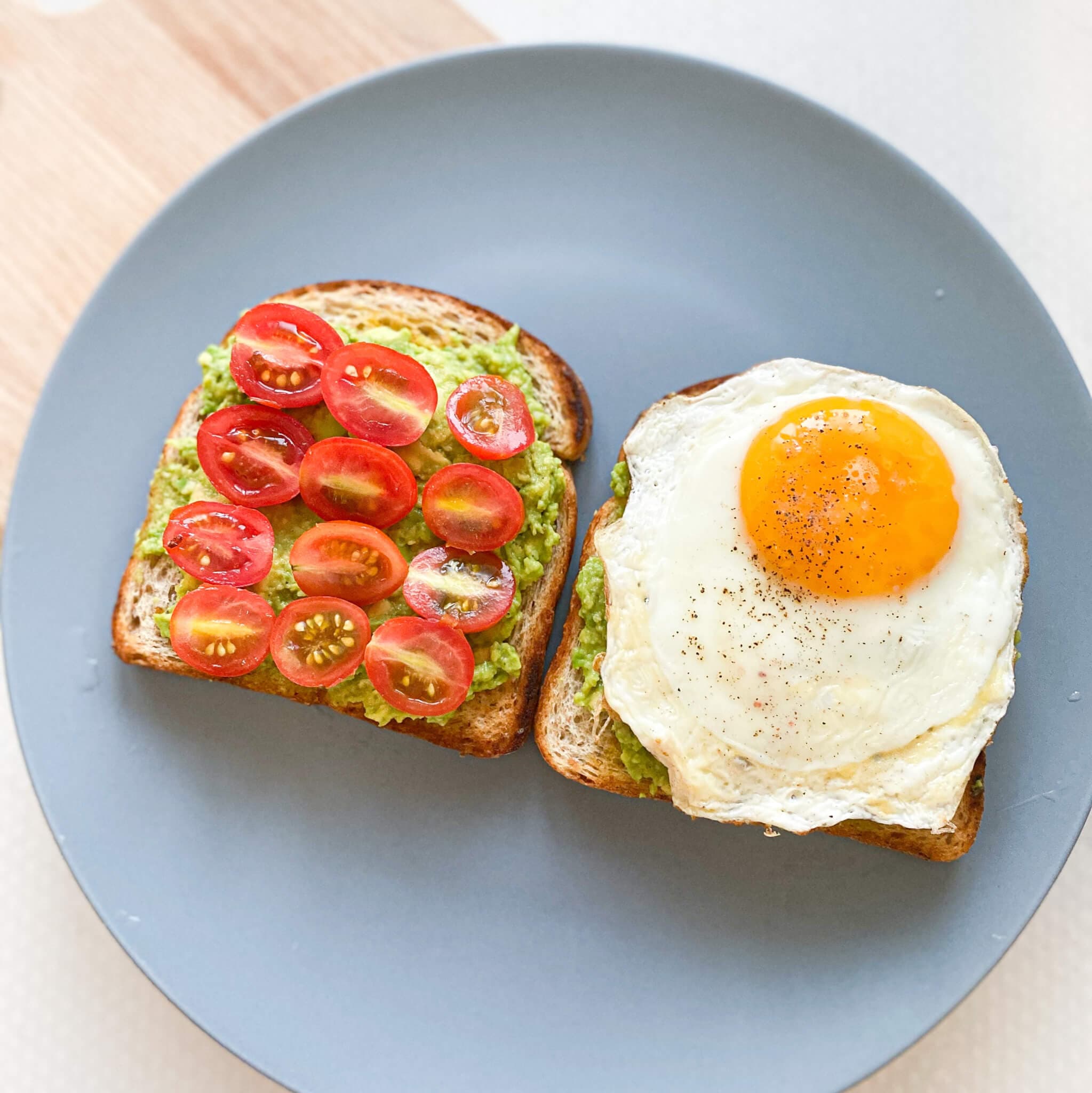Two avocado toasts on a plate; one with sliced cherry tomatoes and the other topped with a sunny-side-up egg. - Home Instead