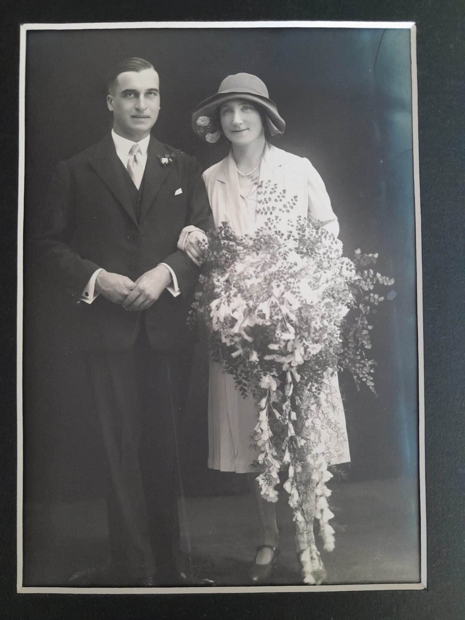 A vintage photo of a bride holding a large bouquet and a groom standing beside her, both in formal attire. - Home Instead