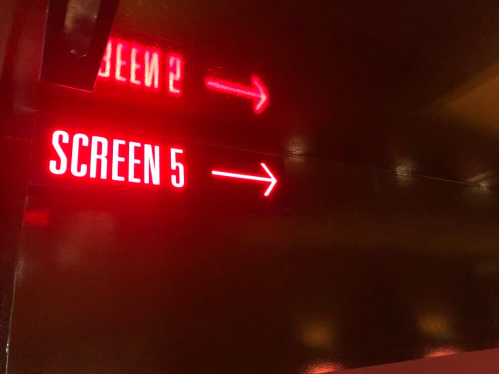 Red neon sign pointing to "Screen 5" with an arrow indicating direction against a dark background. - Home Instead