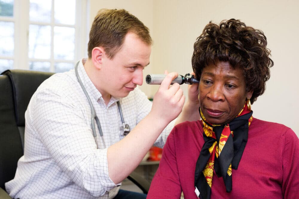 Doctor examining a patient's ear with an otoscope during a checkup in a medical office. - Home Instead