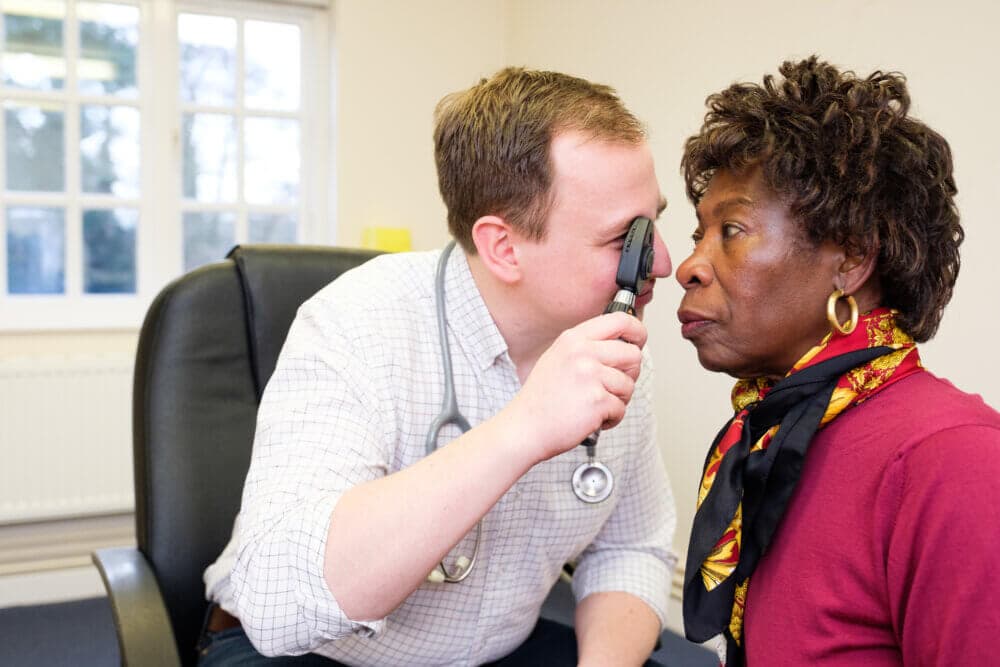 Doctor examining an elderly woman's eye in a medical office with an ophthalmoscope. - Home Instead