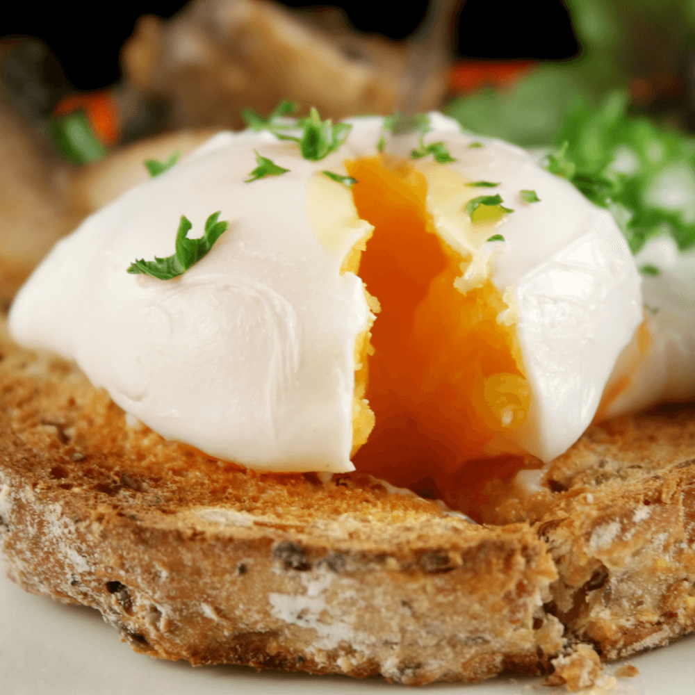 Close-up of a poached egg with a runny yolk on toasted bread, garnished with parsley. - Home Instead