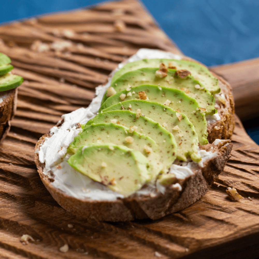 Toast with cream cheese, sliced avocado, and a sprinkle of seasoning on a wooden board. - Home Instead