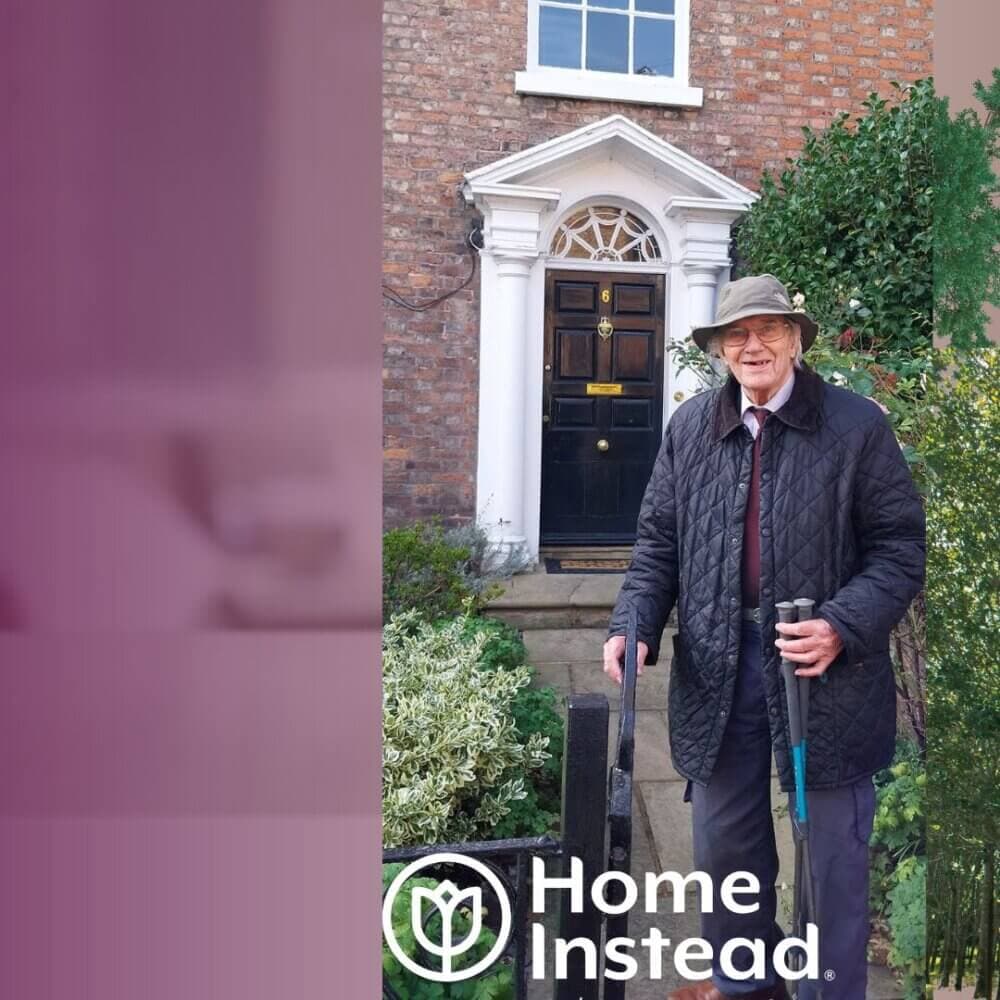 Elderly man wearing a hat and coat, holding walking aids, smiling in front of a house with the "Home Instead" logo. - Home Instead
