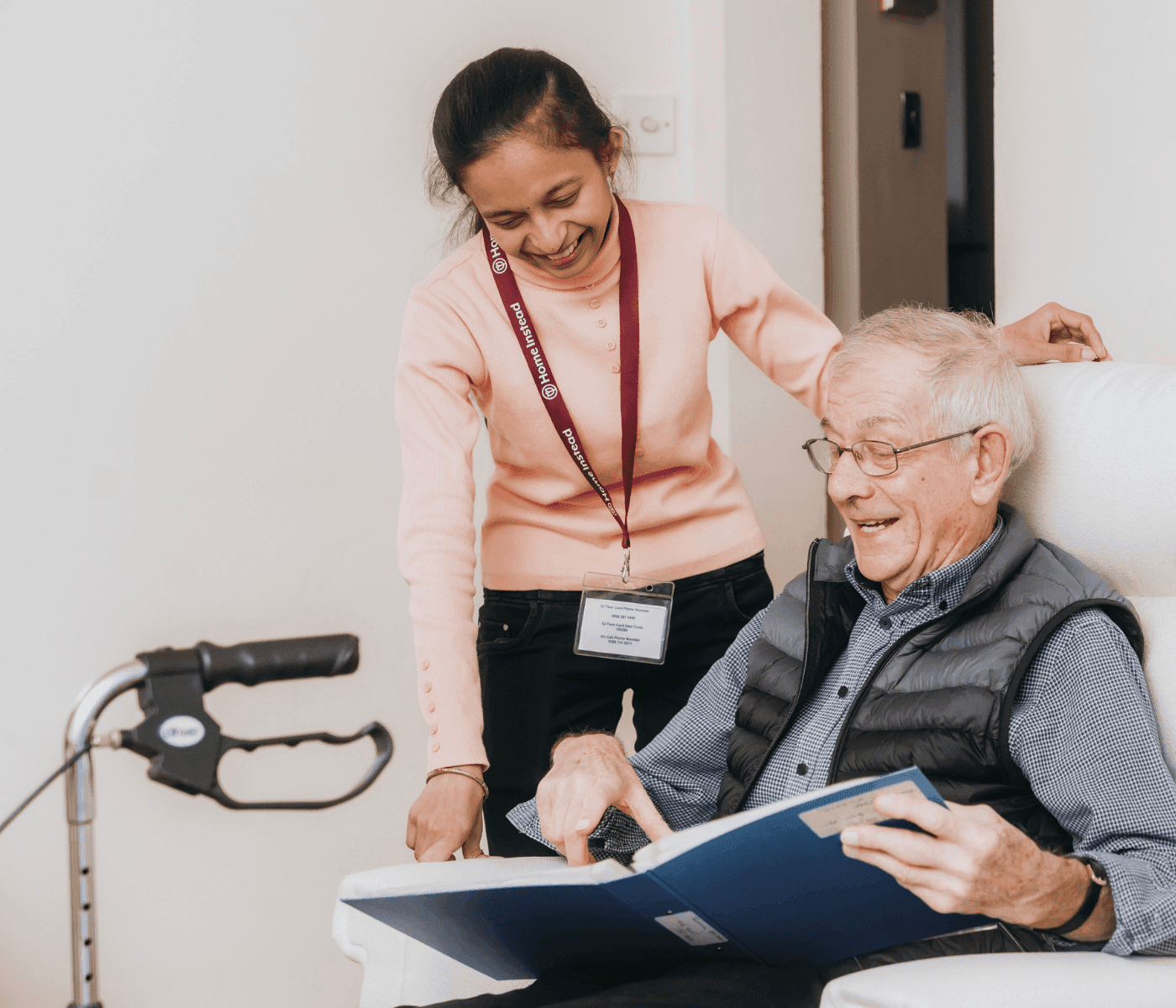 Caregiver helps elderly man reading a book while using a walker. - Home Instead