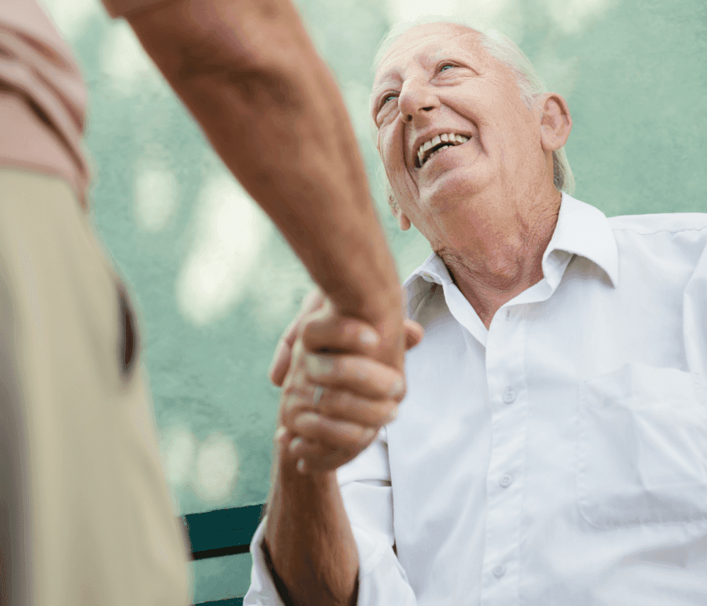 Elderly man smiling and shaking hands with another person outdoors. - Home Instead