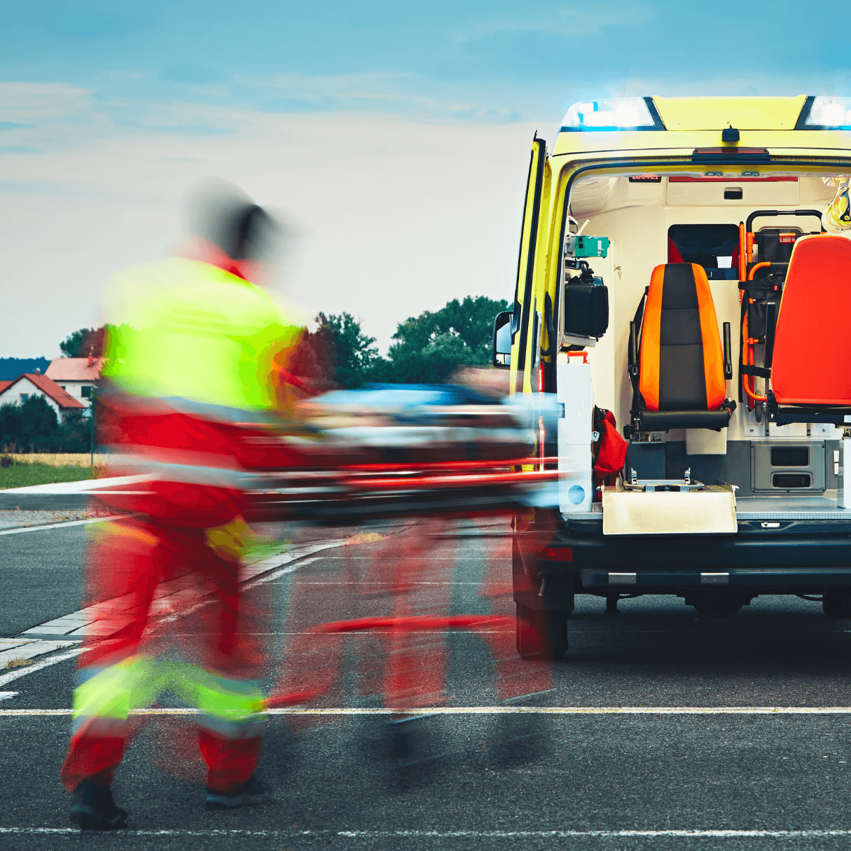 Emergency responders lift a patient on a stretcher into the back of an ambulance on a road. - Home Instead