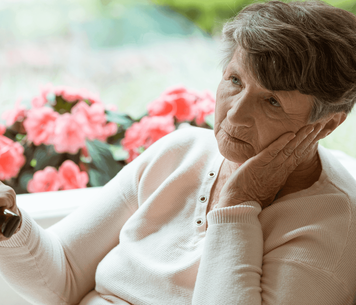 Elderly woman with a pensive expression sitting and resting her head on her hand, with pink flowers in the background. - Home Instead