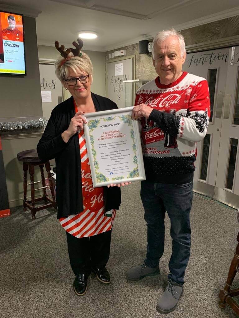 Two people holding a framed certificate, one in a reindeer headband, the other in a Coca-Cola sweater. - Home Instead