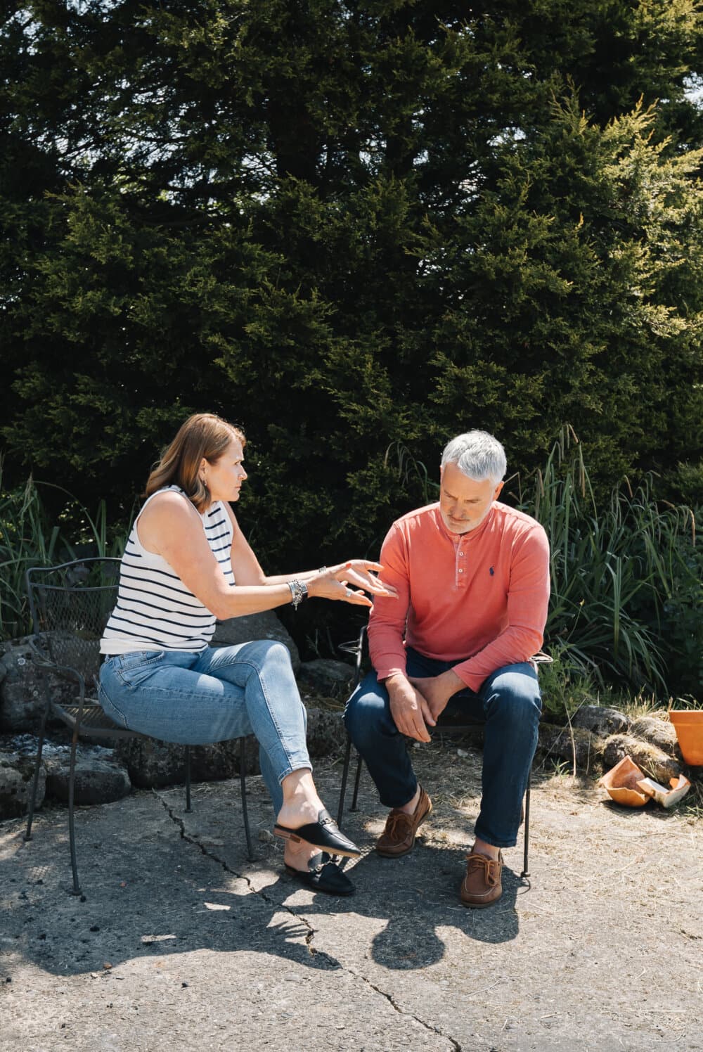 A woman gestures while talking to a man sitting next to her in an outdoor setting with greenery in the background. - Home Instead