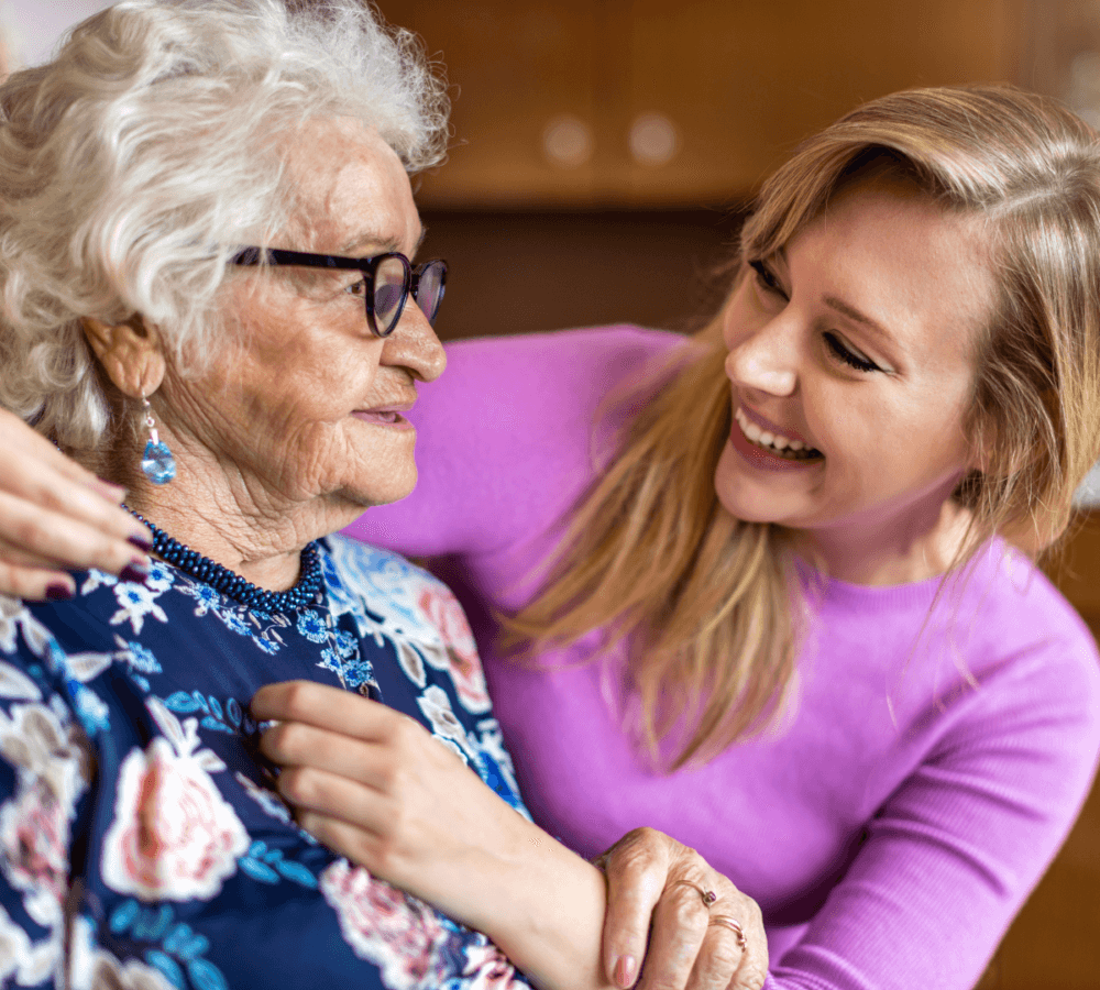 Elderly woman and young woman smiling at each other, showing affection and warmth. - Home Instead