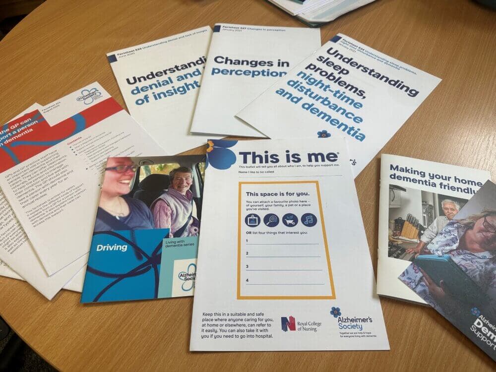 A variety of informational pamphlets and booklets about dementia are spread out on a table. - Home Instead