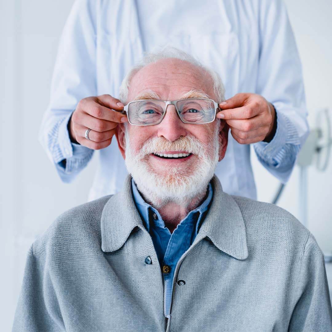 senior man smiling with new glasses being placed on his face