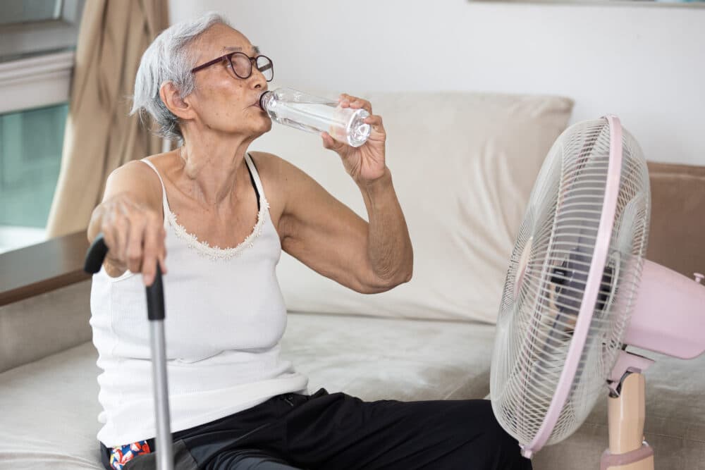 keep cool in summer woman drinking water sitting on her bed home instead