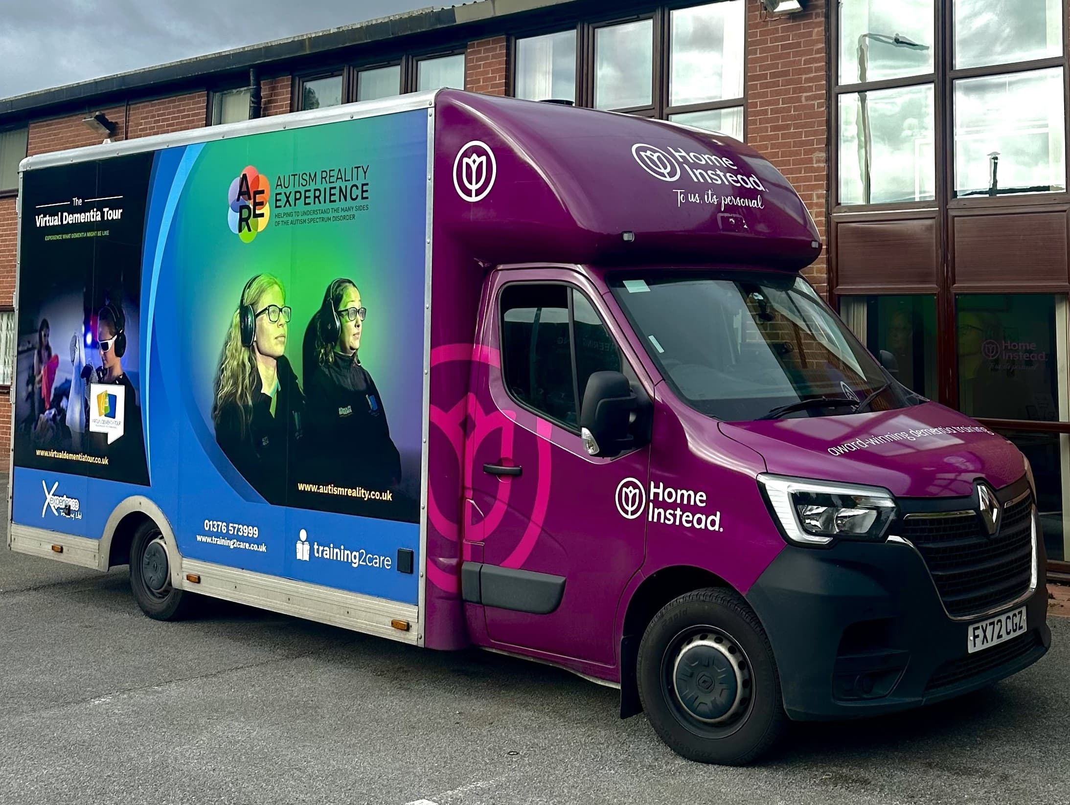 A purple and blue van with "Autism Reality Experience" and "Home Instead" branding, parked outside a building. - Home Instead