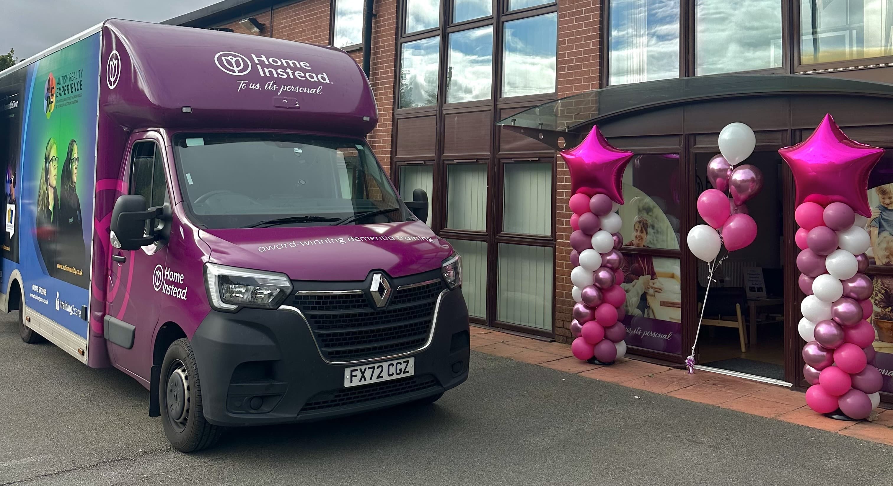 A purple Home Instead van parked outside a building with pink and white balloon decorations at the entrance. - Home Instead