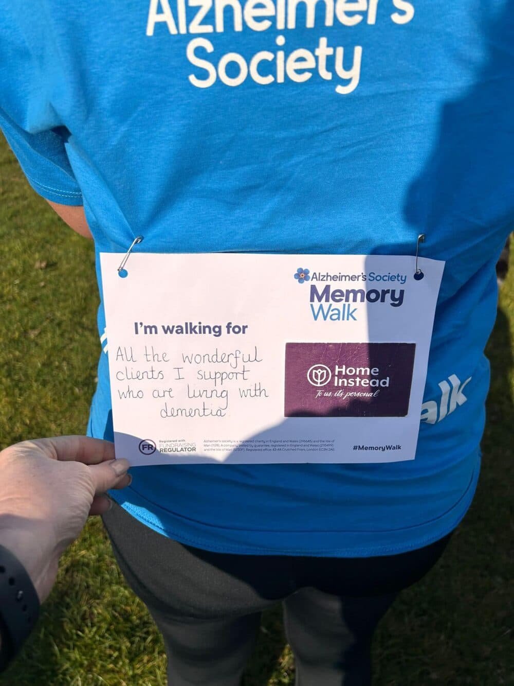 The back of Vicki's t-shirt, showing the label stating she is walking for 'All the wonderful clients she supports who are living with Dementia', with the Home Instead logo to the side.