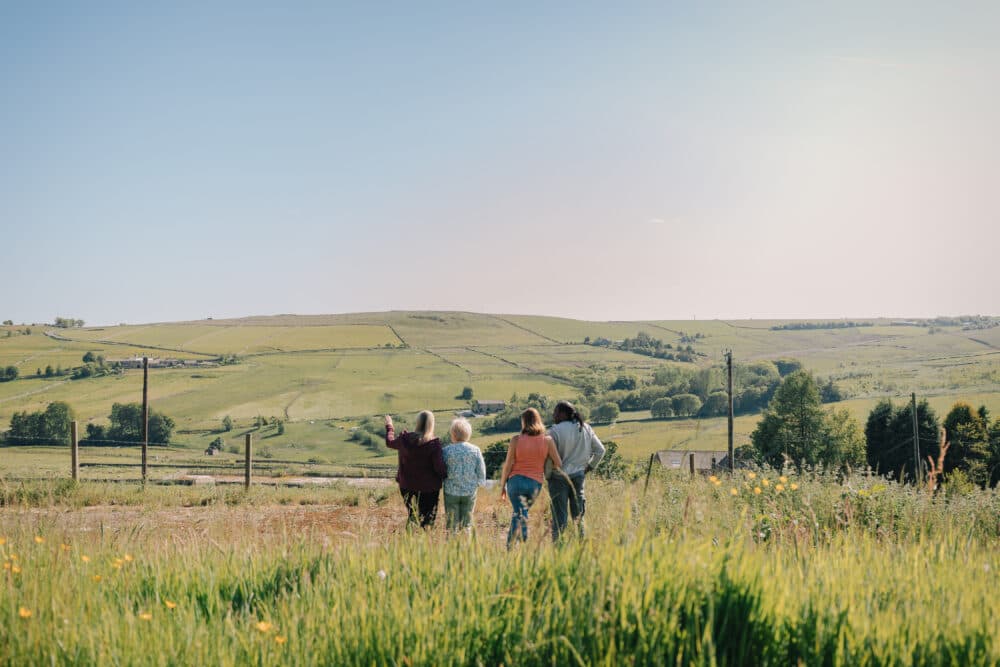 Four people walking through a grassy field, overlooking rolling hills under a clear blue sky. - Home Instead