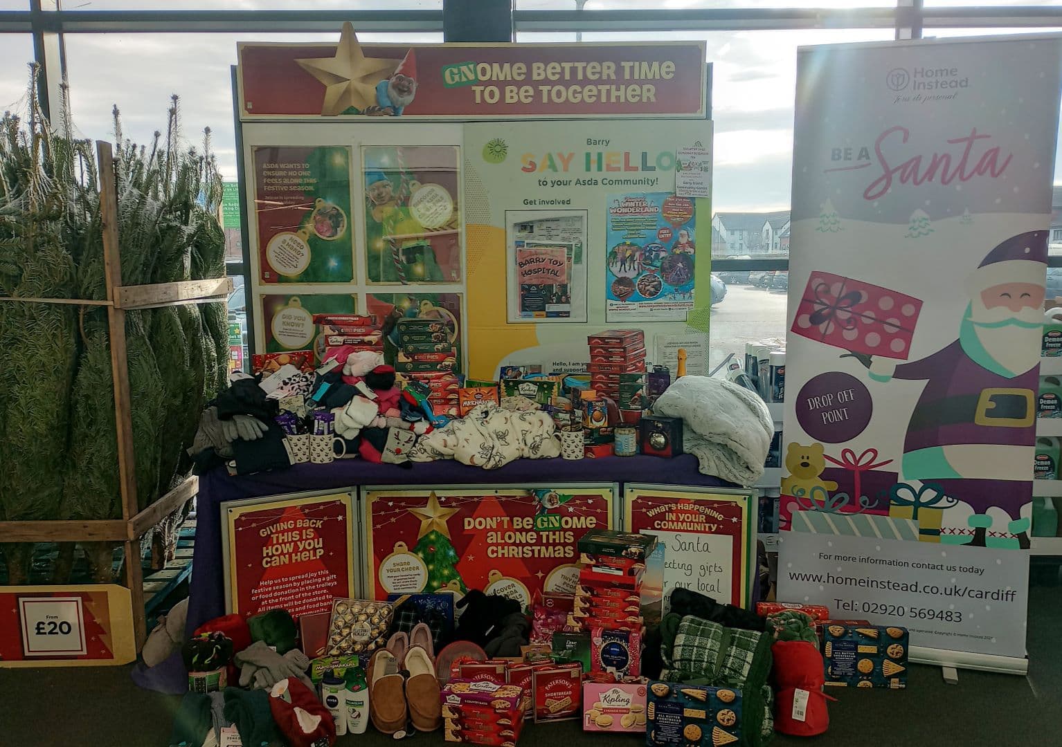 A festive display with Christmas trees, gifts, hats, and socks for a holiday charity donation drive. - Home Instead