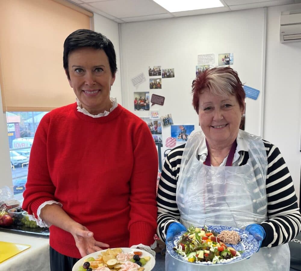 Two women smiling while holding a plate with food inside the office