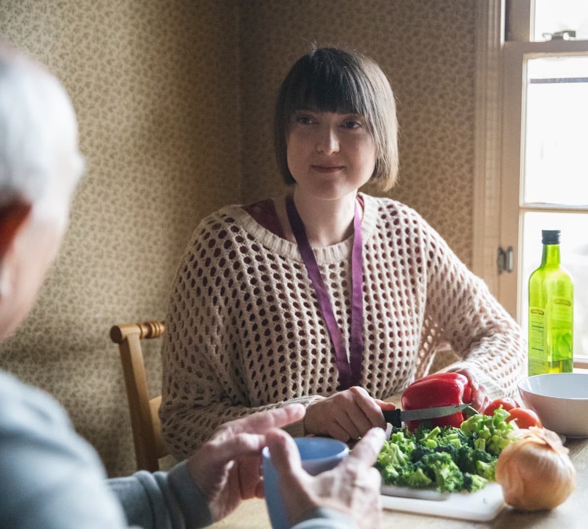 Woman with short hair sitting down and smiling while cutting some vegetables