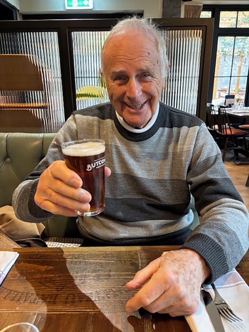 Male client out for a pub lunch holding up a pint of beer and wearing a striped jumper.