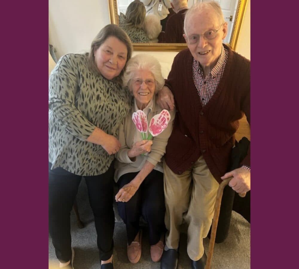Happy Family photo with older woman holding flowers in the middle all happy and smiling inside the home