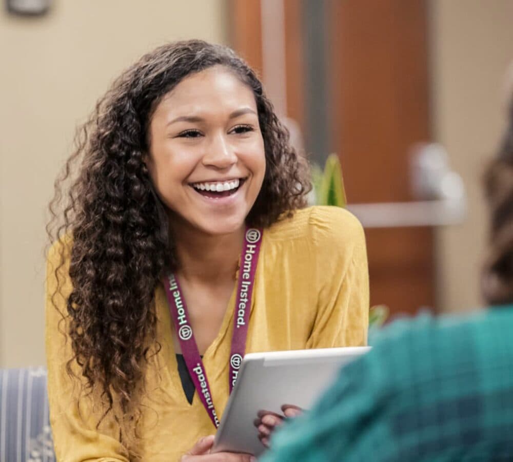 A younger woman wearing mustard top and an ID lanyard with long curly hair happy and smiling