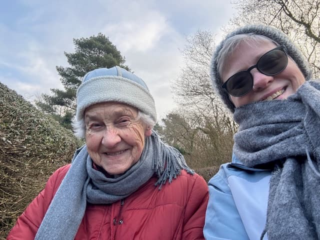 Elderly client in hat and scarf with carer also in hat and scarf with dark glasses on.