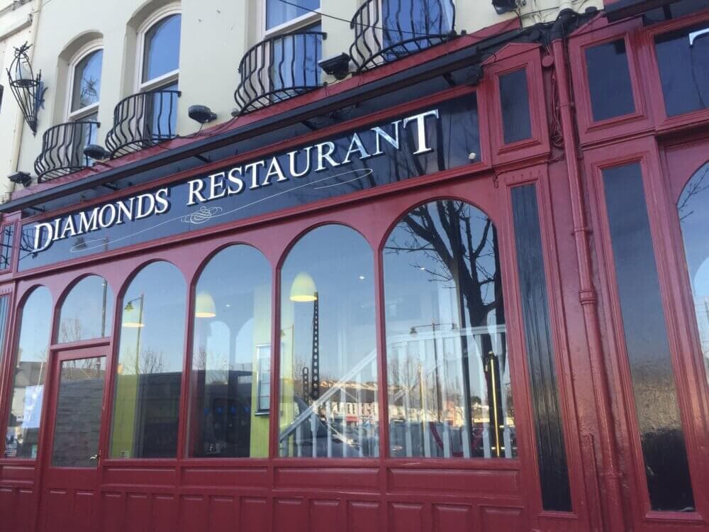Red and black exterior of Diamonds Restaurant with arched windows reflecting the street scene. - Home Instead