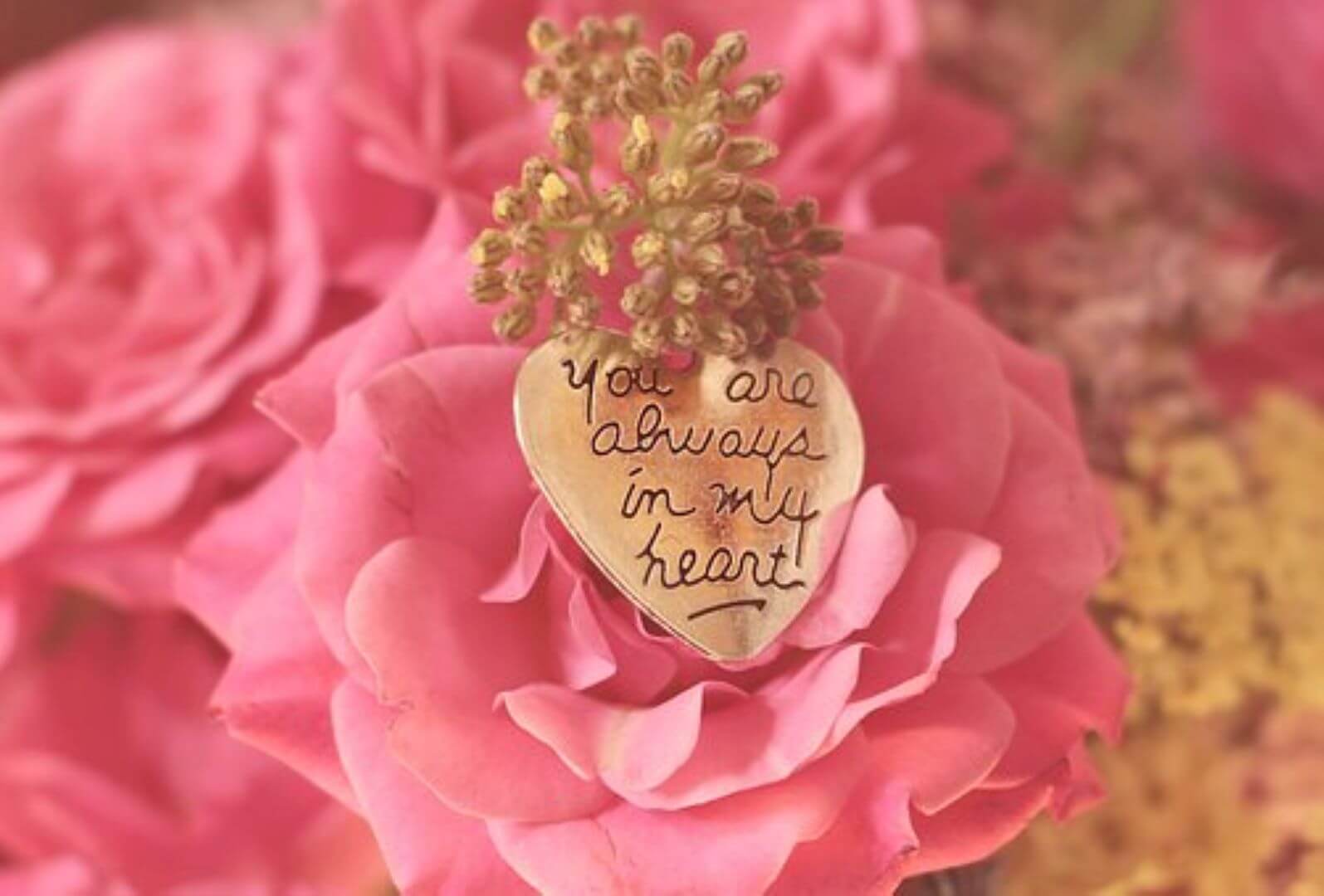 A heart-shaped pendant with "You are always in my heart" inscribed, placed on pink roses with delicate blossoms. - Home Instead
